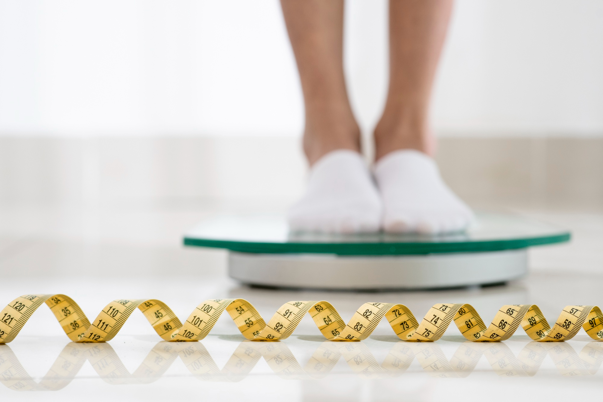 A man standing on a weighing scale with a measuring tape in front, illustrating whether insulin resistance causes weight gain.