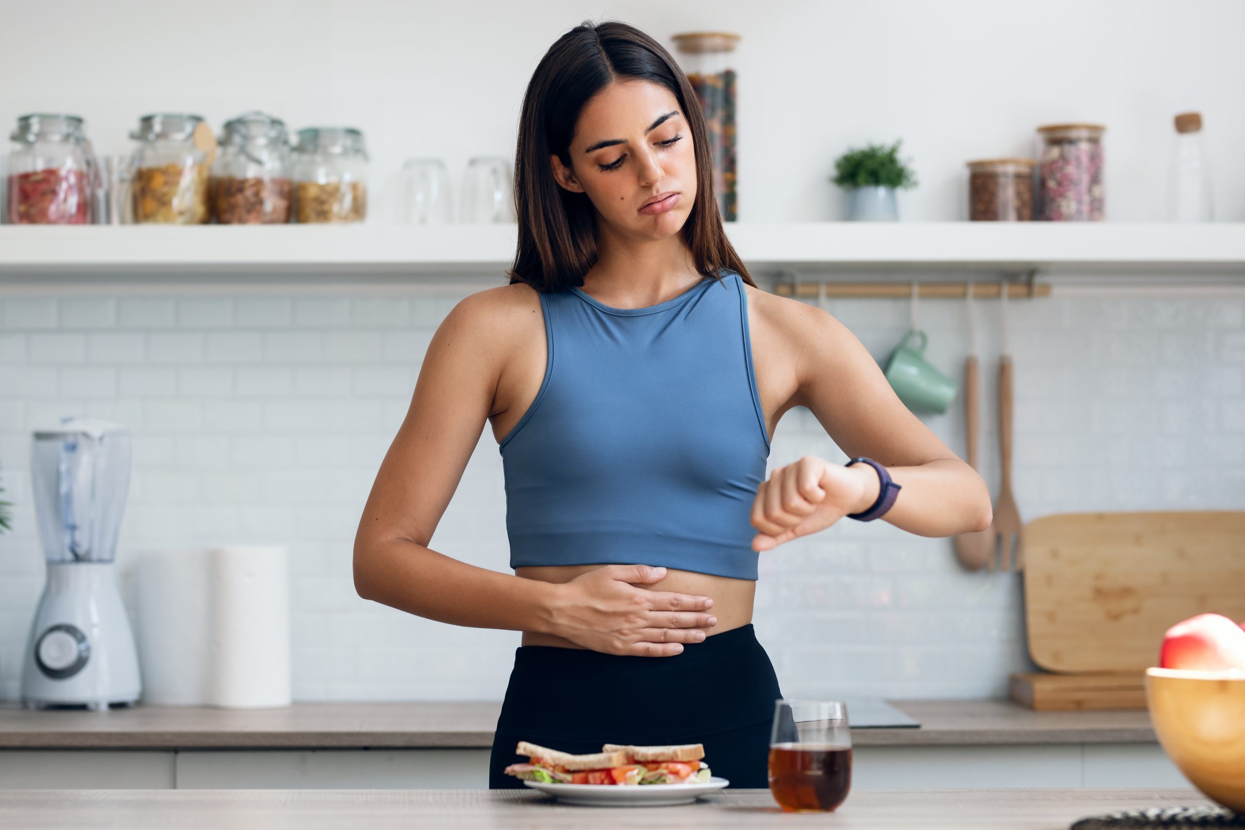 A fit woman touching her belly with breakfast on the table, illustrating how insulin can increase hunger and appetite management.