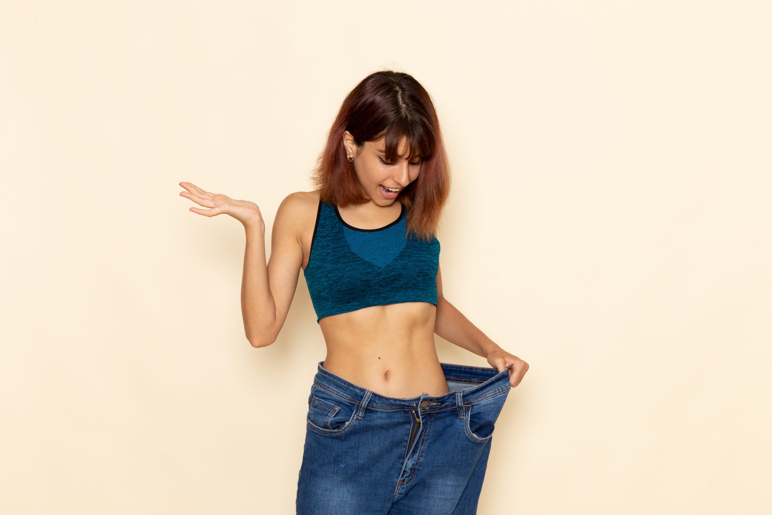 A smiling woman pulling her loose jeans waistband, illustrating when semaglutide starts working for weight loss and what to expect.